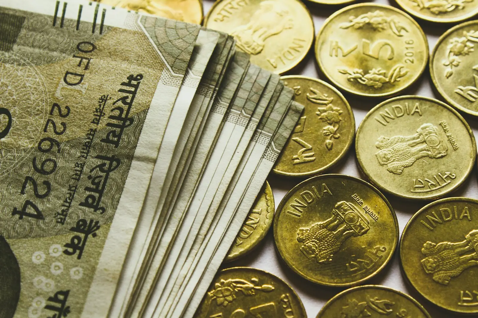 Indian rupee banknotes fanned out beside a row of gold-coloured five-rupee coins