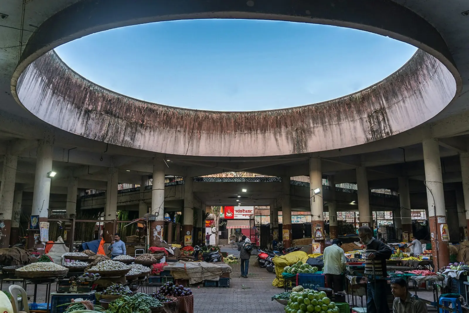 The interior of a large covered Indian wholesale vegetable market with vendors, crates and produce under a domed skylight