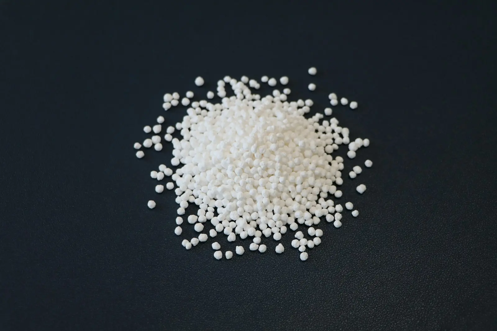 A pile of white urea granules spilling across a dark surface
