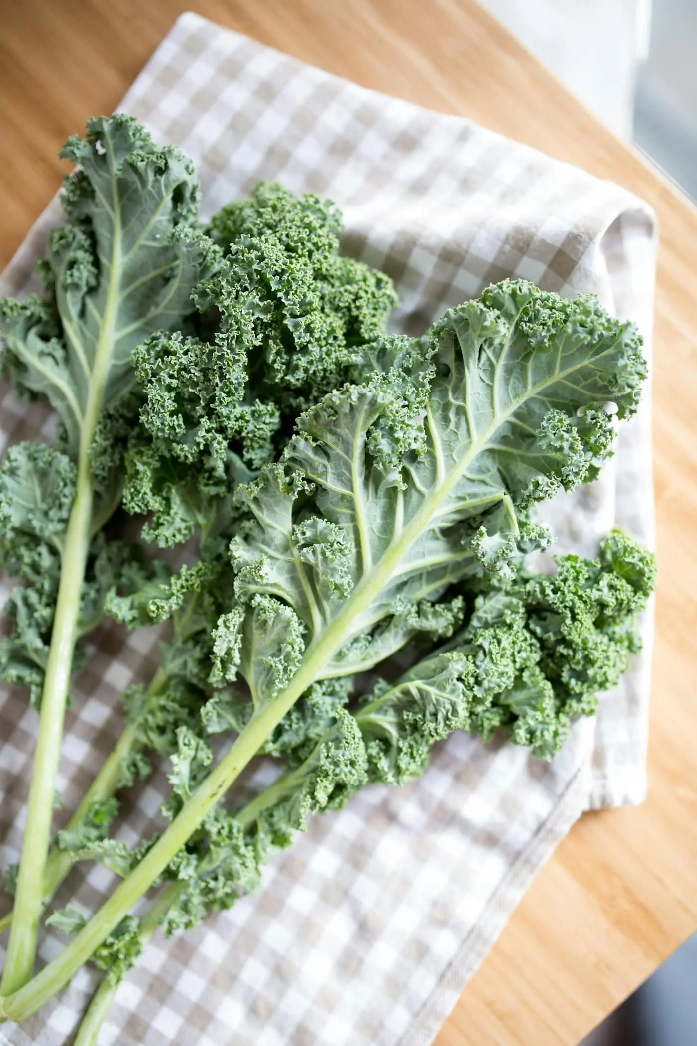 A bunch of fresh curly kale leaves with pale stalks laid on a checked cloth