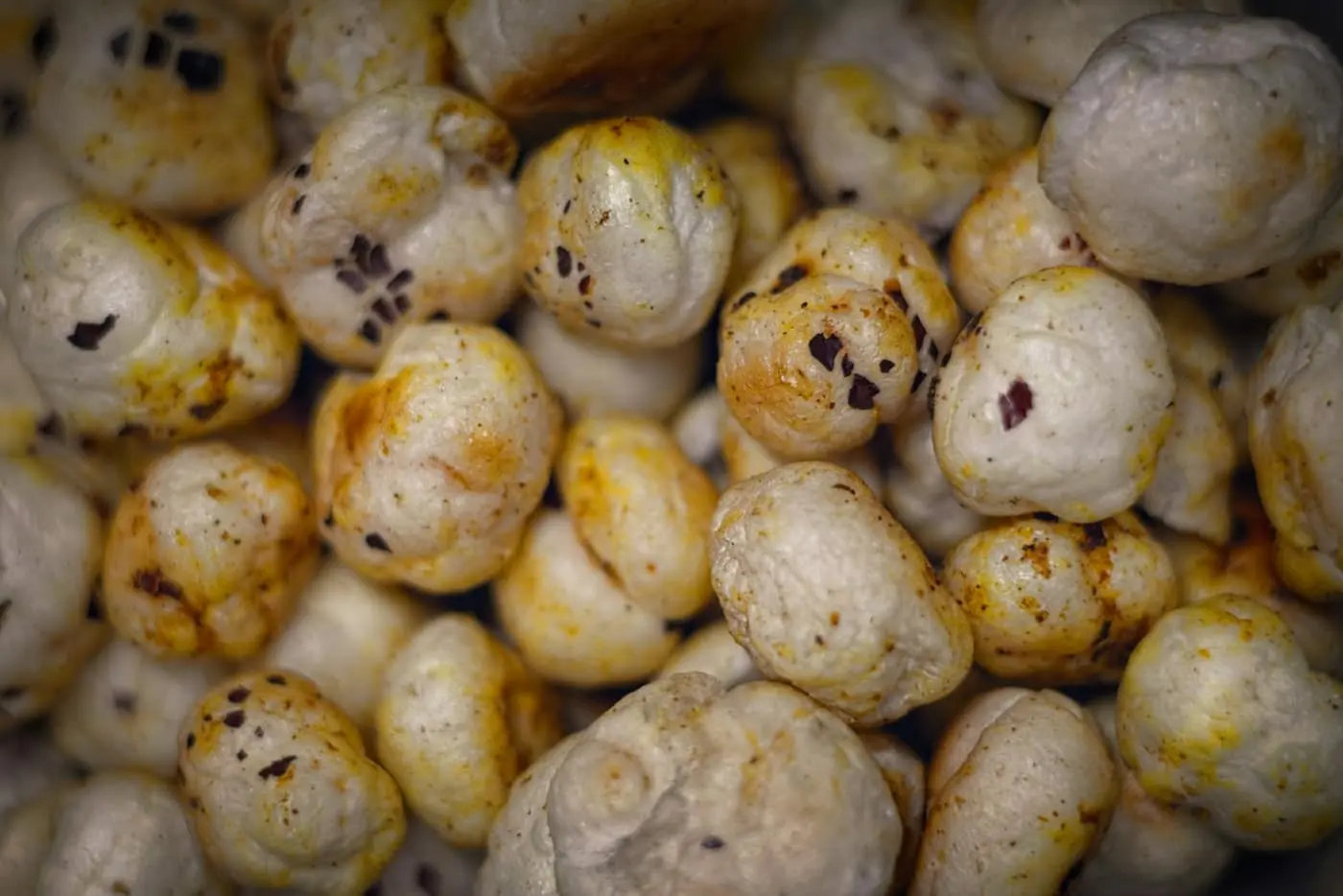 A close-up macro shot of puffed cream-white makhana (fox nut) pieces clustered together, with roasted brown speckling on their popped, textured surface