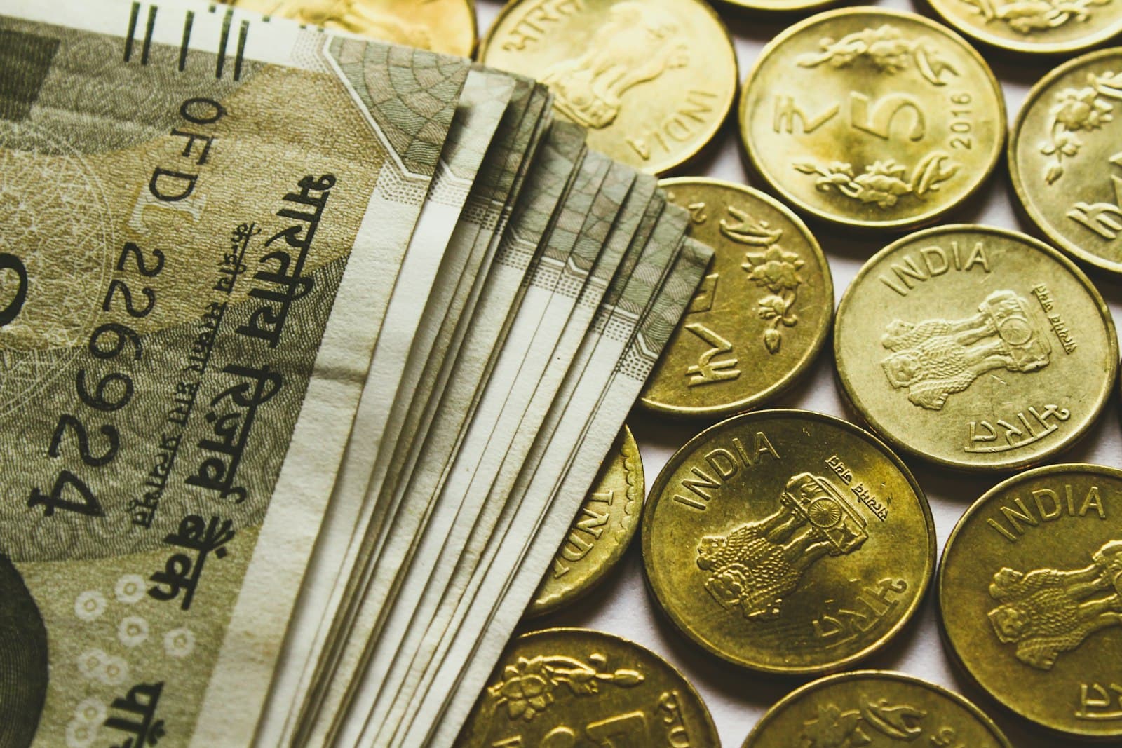 Indian rupee banknotes fanned out beside a row of gold-coloured five-rupee coins