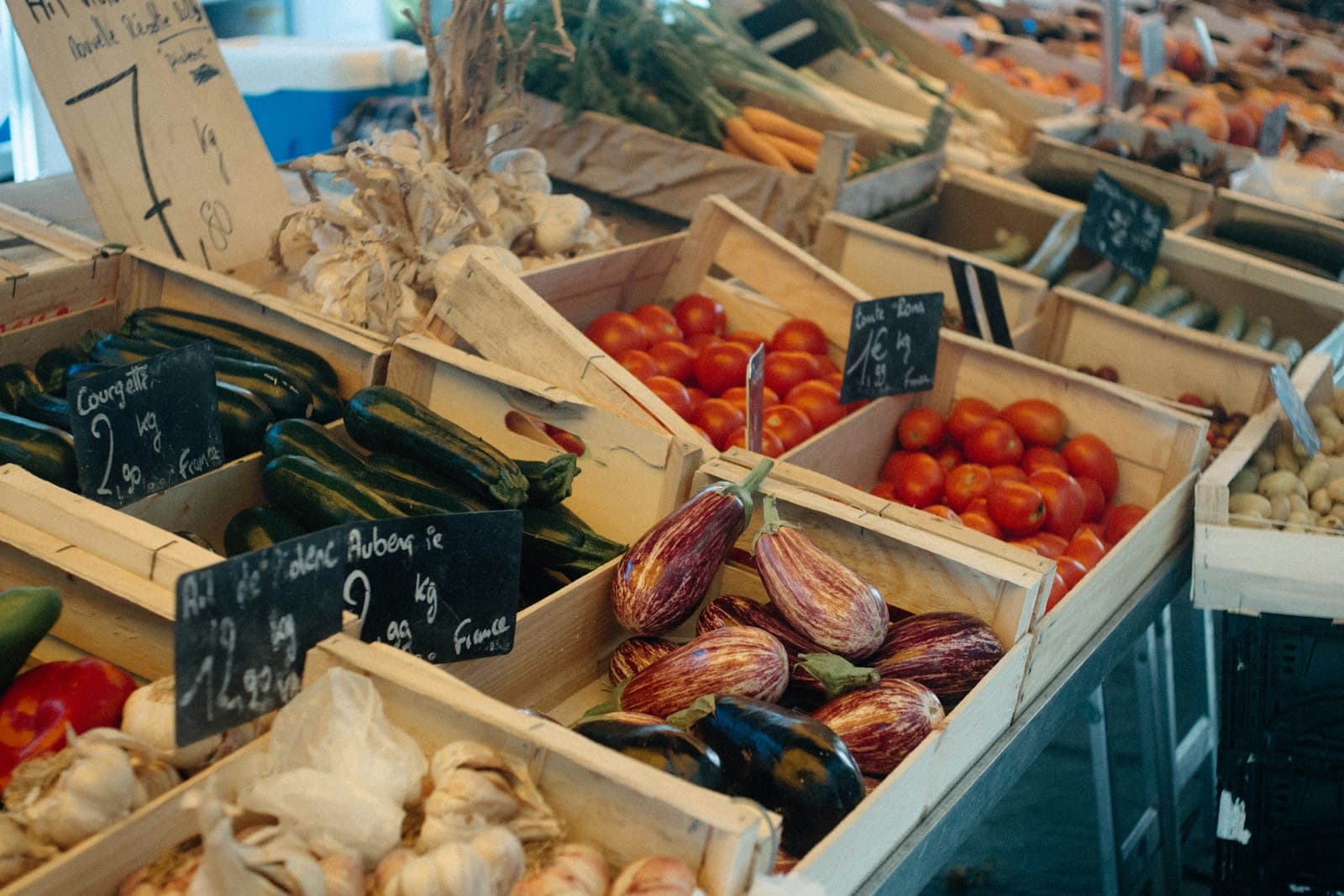 Fresh vegetables including tomatoes, courgettes and aubergines displayed in wooden crates at an outdoor market stall