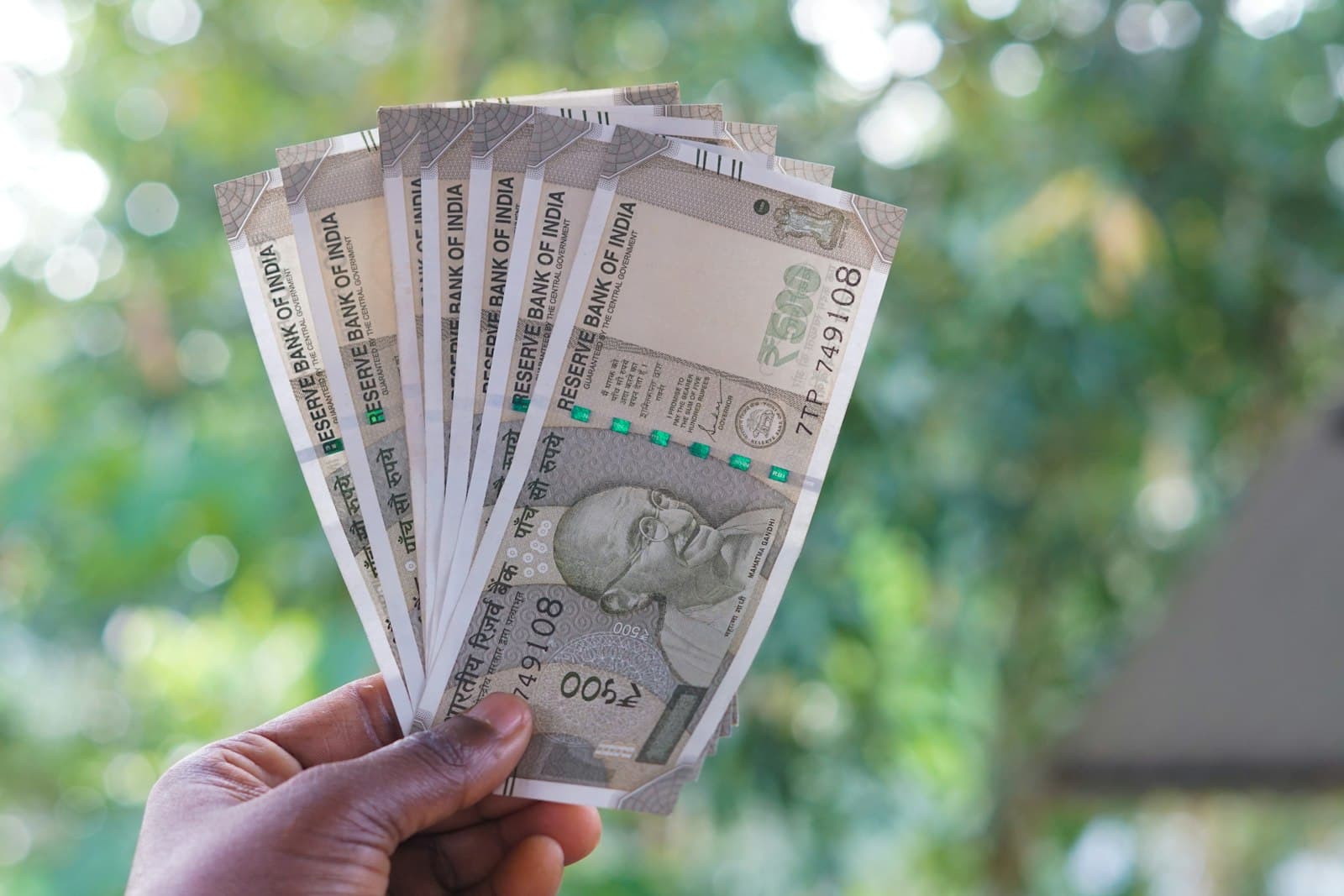 A hand fanning out several Indian ₹500 rupee notes outdoors