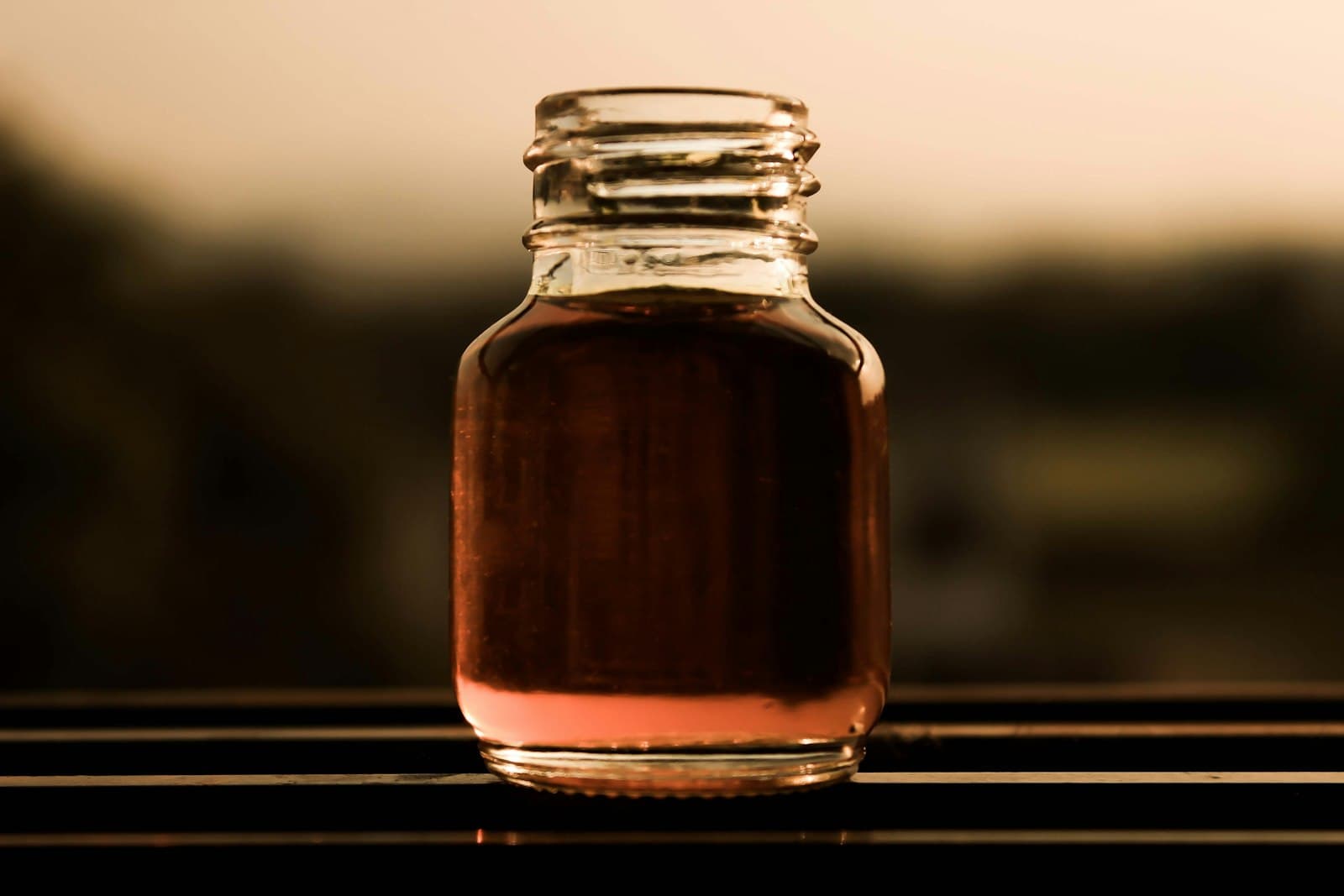 A glass jar of amber liquid backlit by warm evening light