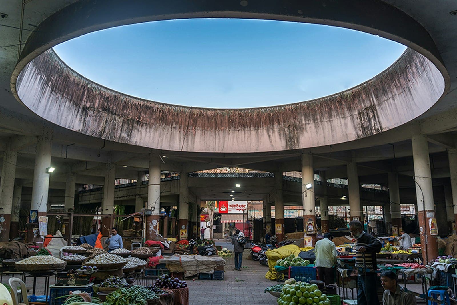 The interior of a large covered Indian wholesale vegetable market with vendors, crates and produce under a domed skylight