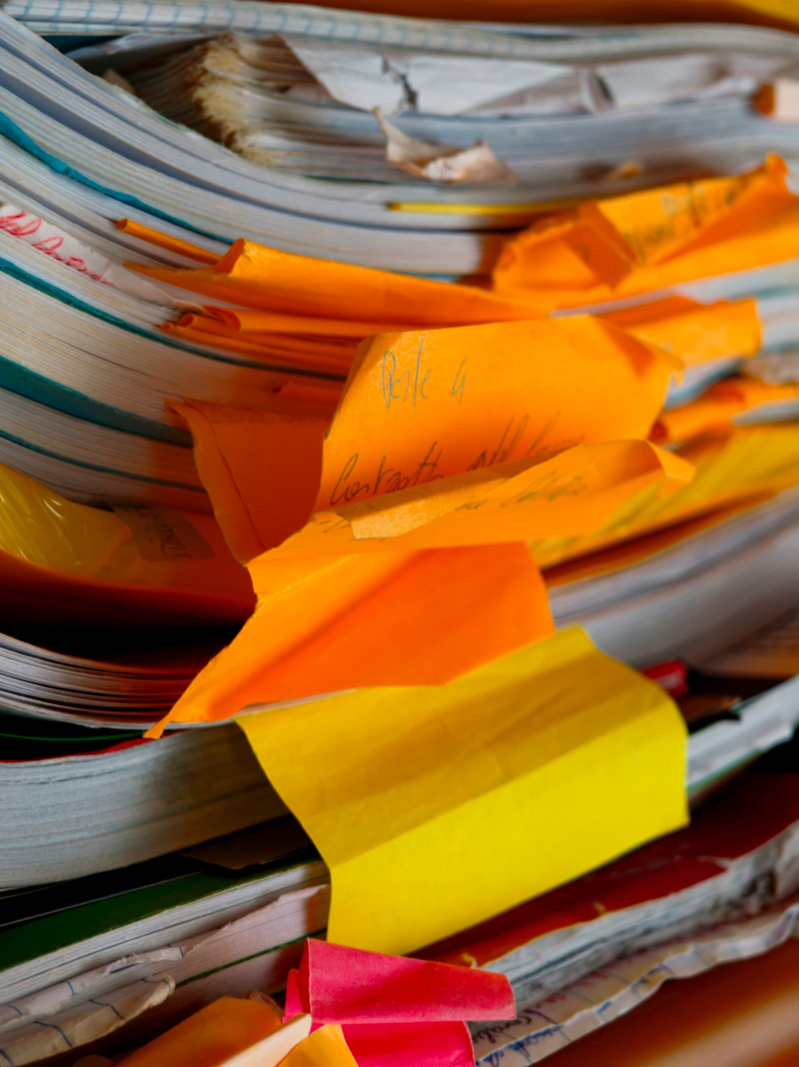 A tightly packed stack of old exercise books and files, with torn orange and yellow paper tabs sticking out between the pages