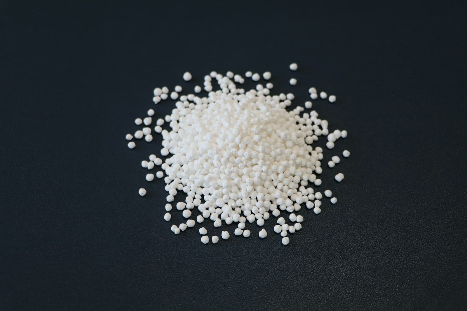 A pile of white urea granules spilling across a dark surface