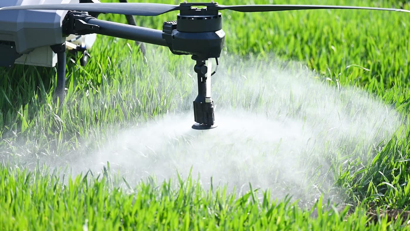 Close-up of an agricultural drone’s spray nozzle releasing a fine mist over a green wheat field