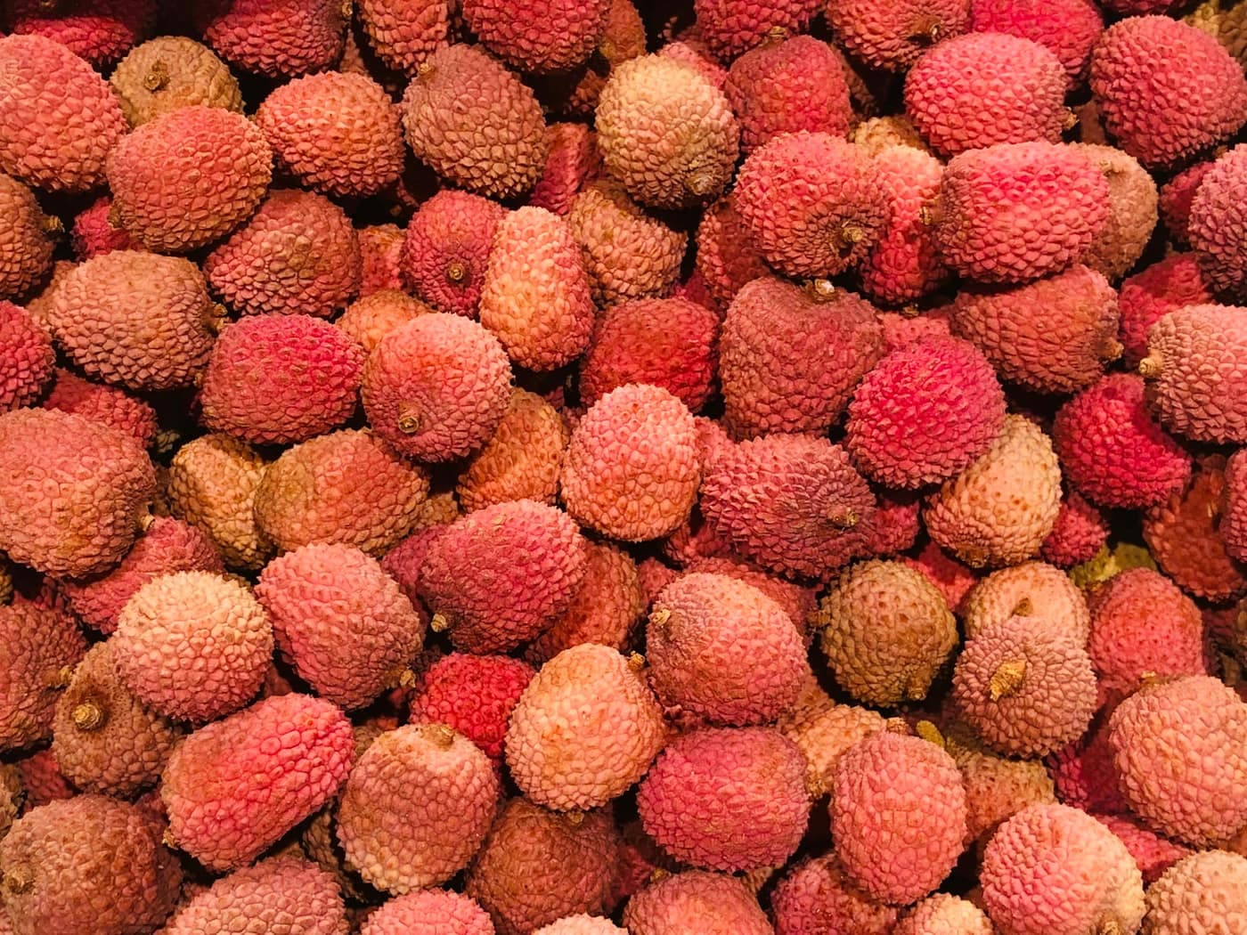 A pile of fresh pink-red, rough-skinned litchi fruits