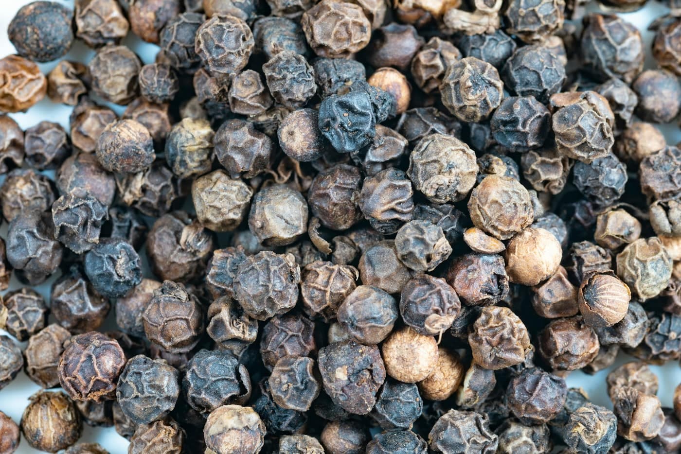 A close-up macro pile of dried black peppercorns, showing the wrinkled, reticulated skin of each spherical corn