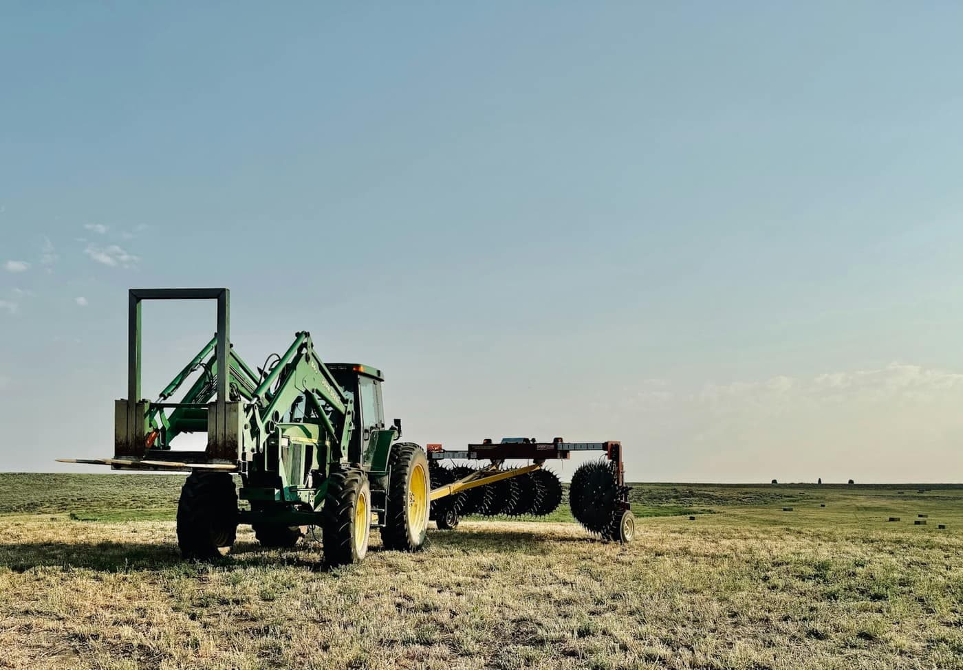 A tractor towing a disc harrow with its round blades visible, parked in a stubble field