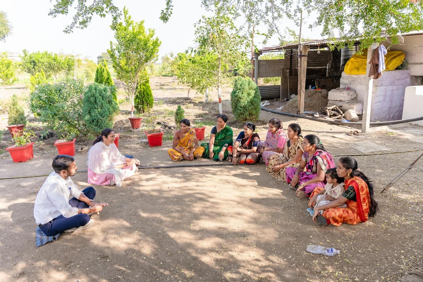 Two facilitators lead a group discussion with about ten women farmers seated in a circle in the shade of a tree outside a farmhouse in Nagpur, Maharashtra — the kind of village meeting a CBBO holds to mobilise and register a new FPO