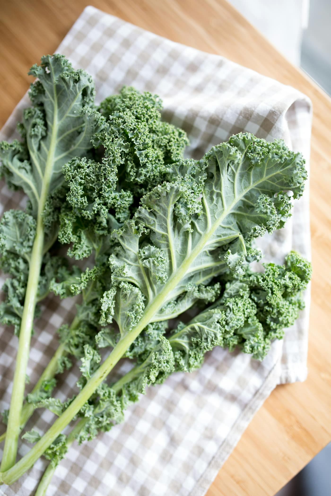 A bunch of fresh curly kale leaves with pale stalks laid on a checked cloth
