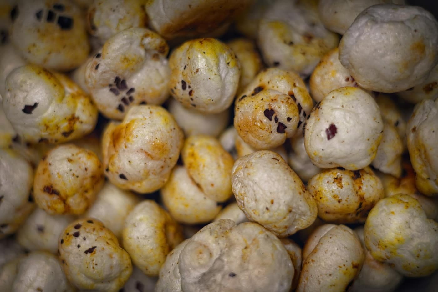 A close-up macro shot of puffed cream-white makhana (fox nut) pieces clustered together, with roasted brown speckling on their popped, textured surface
