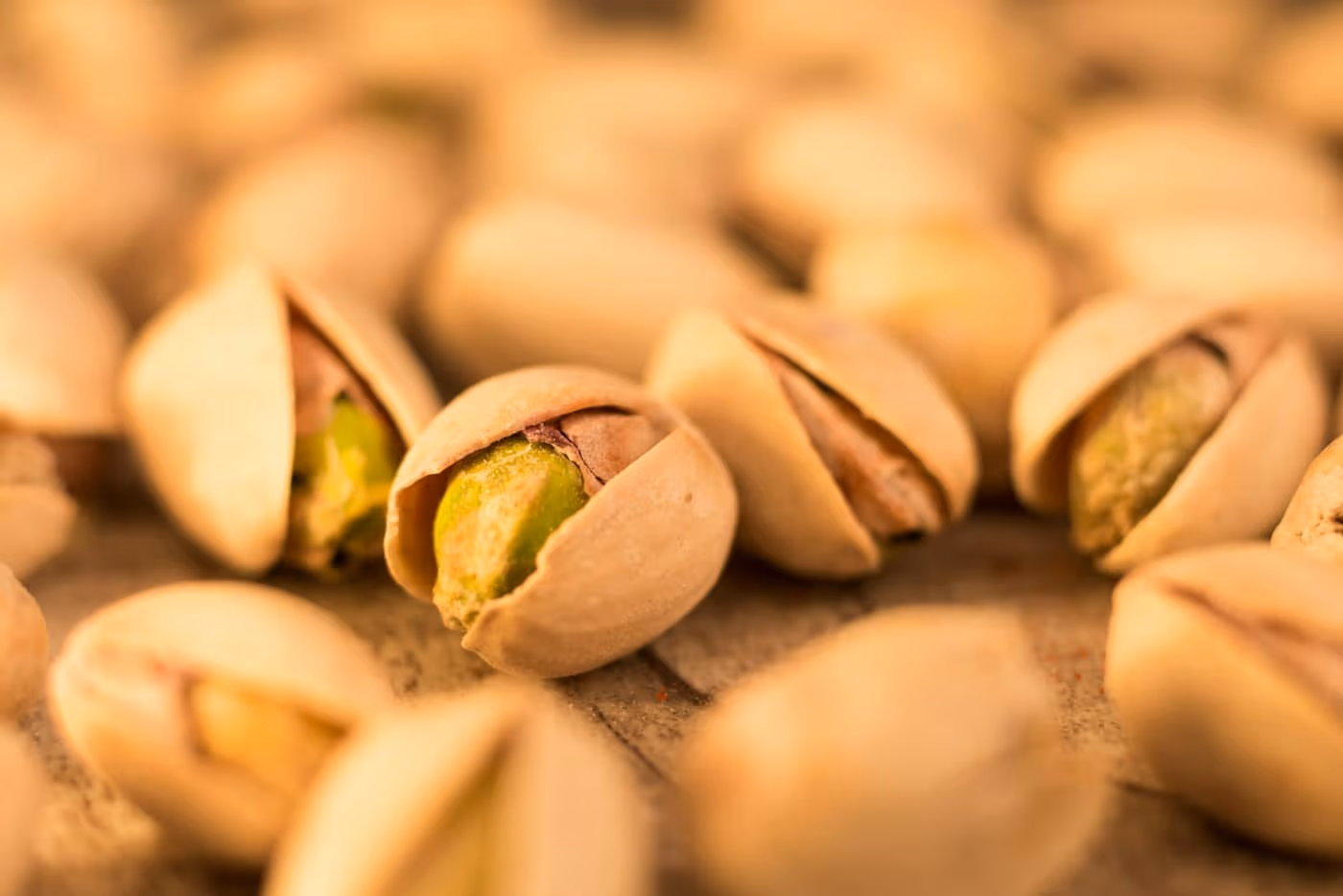 A close-up pile of split-open, in-shell pistachio nuts showing the pale shell and green kernel inside
