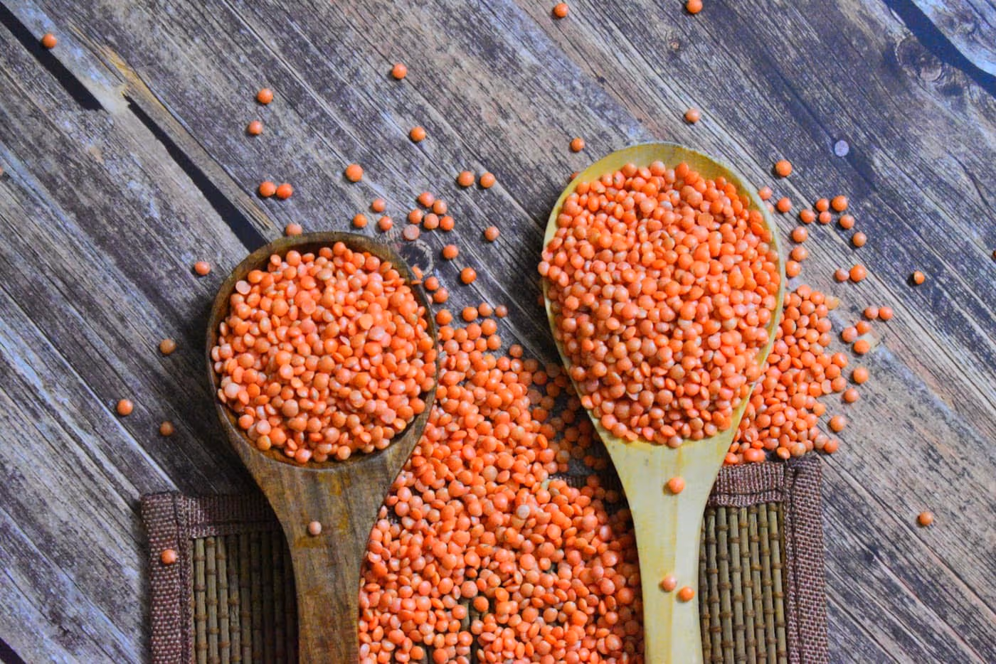 Two wooden spoons piled high with red lentils, spilling across a weathered wooden table