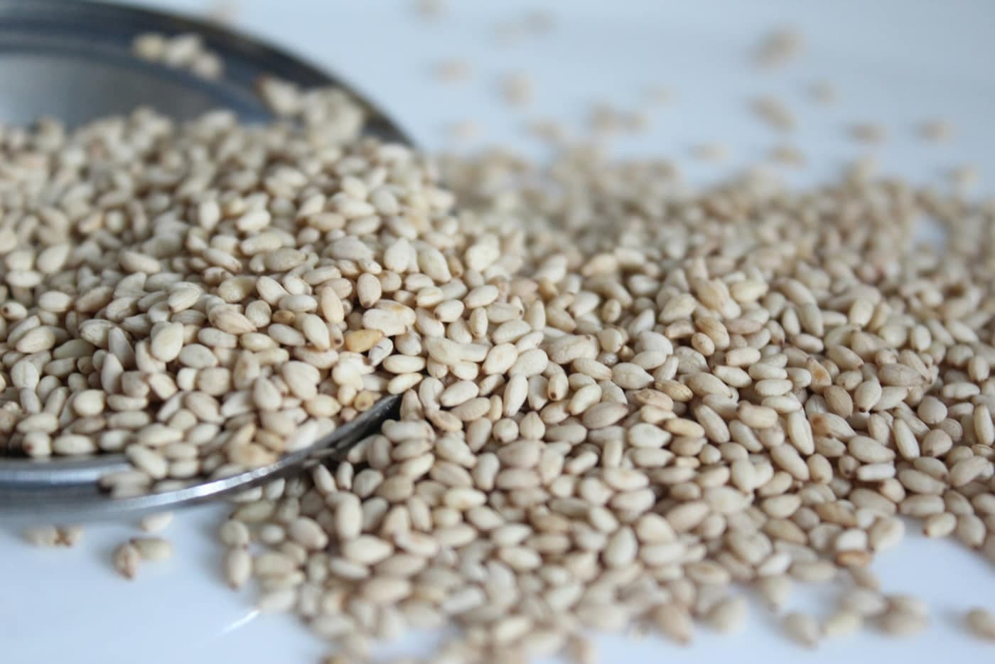 Pale sesame (til) seeds spilling from a steel plate onto a white surface