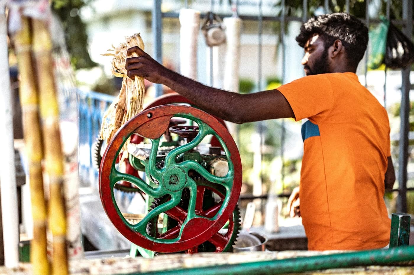 A young man feeding sugarcane stalks into a hand-cranked sugarcane-juice extraction machine at a roadside stall