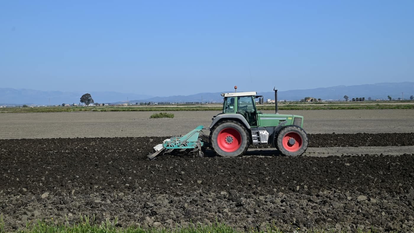 A tractor towing a cultivator implement across freshly turned soil