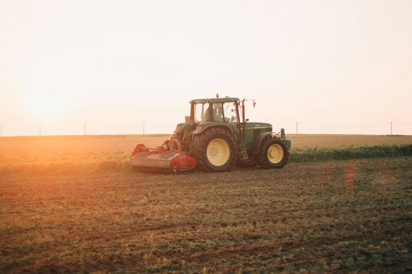 A tractor towing a wide, low implement across a field at sunset